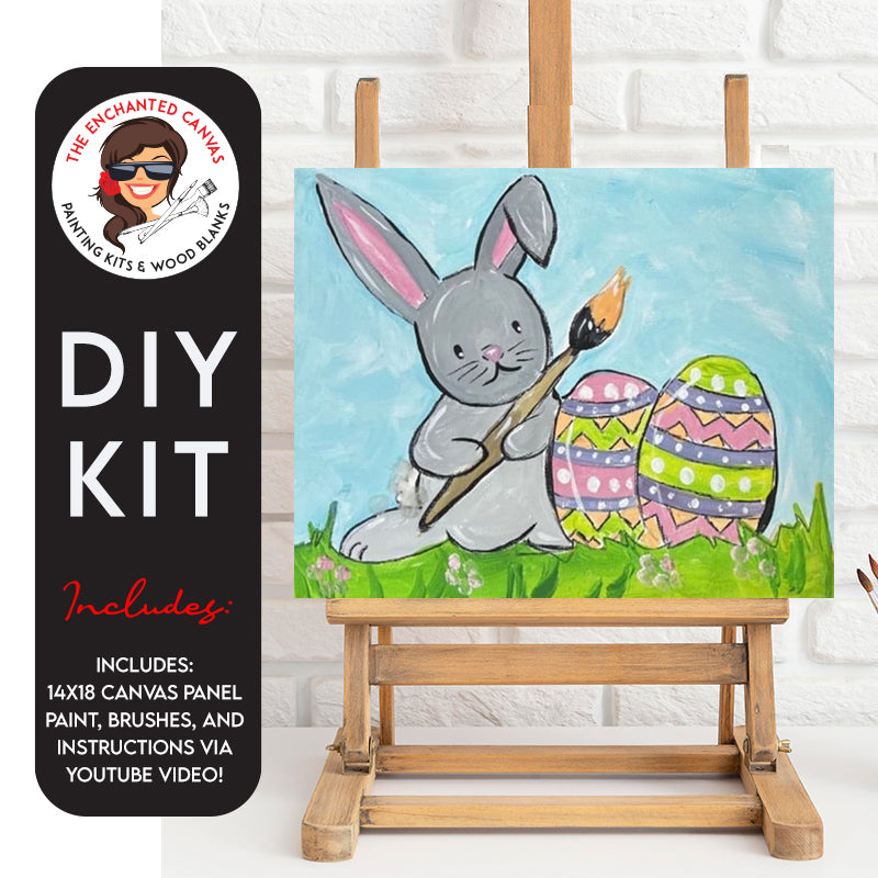 Cute little grey bunny is holding a paintbrush with orange paint on the tip. The bunny sits in a field of grass with pink flowers and blue sky. In front of the bunny are easter eggs in various polka dot patterns and stripe zig zag patterns. Various colors of the eggs are used like green, yellow and pinks.